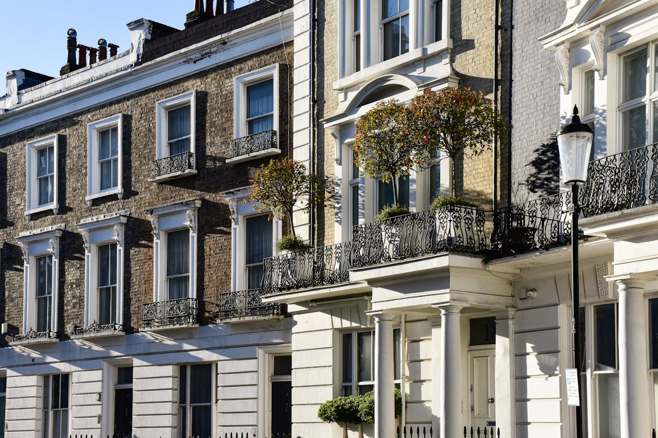 A row of classic London townhouses with detailed iron balconies under a clear blue sky.
